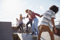 Friends on skateboards holding hands in a row on ramp at sunny skate park — Stock Photo