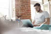 Чоловік використовує ноутбук на ліжку в квартирі — стокове фото