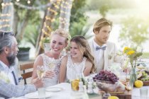 Молодая пара и их гости сидят за столом во время свадебного приема в саду — стоковое фото
