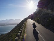 Couple riding motorcycle on sunny road along ocean — Stock Photo