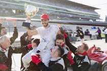 Formula one racing team carrying cheering driver on shoulders, celebrating victory on sports track — Stock Photo