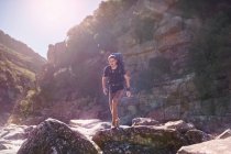 Young man with backpack hiking over sunny rocks — Stock Photo