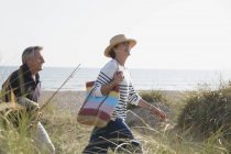 Зріла пара з рибальським стрижнем, що йде на сонячній пляжній траві — стокове фото