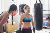 Сміються жінки-боксери поруч з мішками для ударів у спортзалі — стокове фото