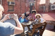 Woman with camera phone photographing friends hanging out on sunny urban rooftop — Stock Photo