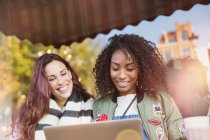 Smiling young women friends using laptop at sidewalk cafe — Stock Photo