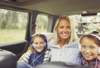 Портрет улыбающейся матери и дочери в наушниках на заднем сиденье автомобиля — стоковое фото
