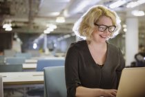 Усміхнена бізнес-леді працює пізно в ноутбуці в темному офісі — стокове фото