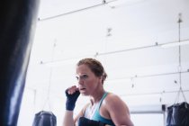 Boxe de boxe féminine déterminée au sac de boxe dans la salle de gym — Photo de stock