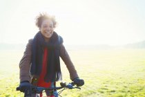 Femme souriante vélo équitation dans l'herbe du parc ensoleillé — Photo de stock