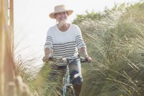 Sonriendo mujer madura montar en bicicleta a lo largo de la hierba de playa - foto de stock
