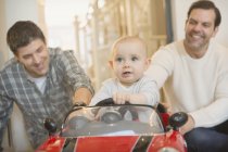 Male gay parents pushing baby son in toy car — Stock Photo