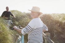 Porträt lächelnde ältere Frau zu Fuß Fahrrad am sonnigen Strand Grasweg — Stockfoto