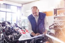 Hombre mayor mecánico de motocicletas revisar los planes en el taller - foto de stock