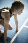 Serious focused female runner ready at starting block on sports track — Stock Photo