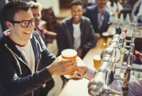 Усміхнений чоловік отримує пиво від бармена в барі — стокове фото