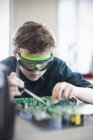 Focused boy student in goggles soldering circuit board in classroom — Stock Photo