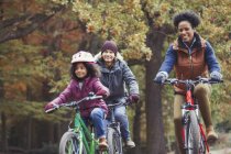 Playful young family bike riding in autumn park — Stock Photo