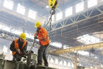 Steel workers fastening crane chain to steel in factory — Stock Photo