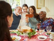Familia multi-étnica multi-generación con teléfono de cámara tomando selfie en la mesa de la cena de Navidad - foto de stock