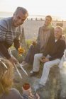 Smiling mature couples drinking wine and barbecuing on sunset beach — Stock Photo