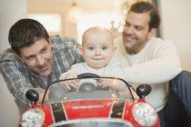 Portrait male gay parents pushing baby son in toy car — Stock Photo