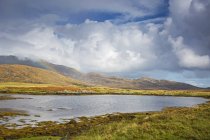 Tranquil view clouds and rainbow over rolling hills beyond lake, Loch Aineort, South Uist, Outer Hebrides — Stock Photo