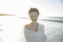 Портрет молодой женщины, завернутой в одеяло на пляже — стоковое фото