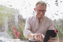 Uomo anziano sorridente utilizzando tablet digitale sul patio — Foto stock