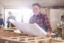 Retrato sorridente carpinteiro masculino rever planos no barco de madeira na oficina — Fotografia de Stock