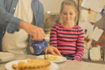 Figlia guardando padre versare crema sopra torta in cucina — Foto stock