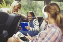 Mãe assistindo filhas com fones de ouvido usando tablets digitais no banco de trás do carro — Fotografia de Stock