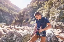 Junger Mann bereitet zwischen sonnigen Felsen Kletterkarabiner und Ausrüstung vor — Stockfoto