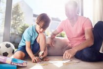 Father and son assembling jigsaw pieces on floor — Stock Photo