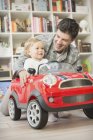 Батько штовхає сина в іграшковий автомобіль — стокове фото