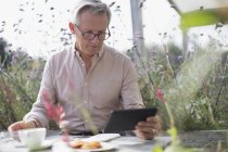 Senior man using digital tablet and drinking coffee at patio table — Stock Photo