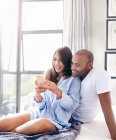 Smiling couple texting with cell phone on bed — Stock Photo