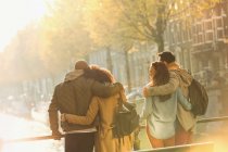 Young couples hugging on bridge over sunny autumn canal, Amsterdam — Stock Photo