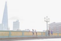 Corredores corriendo y estirándose en el soleado y nebuloso puente urbano, Londres, Reino Unido - foto de stock