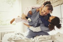Multi-ethnic daughters playing and tackling father on bed — Stock Photo