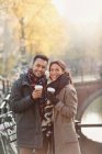 Retrato sonriente joven pareja bebiendo café a lo largo del canal urbano de otoño - foto de stock