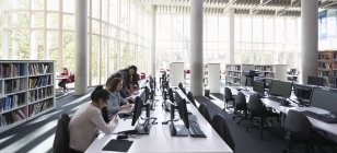 Estudantes pesquisando em computadores na biblioteca — Fotografia de Stock