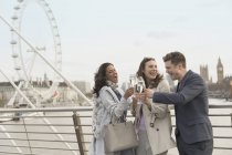 Enthusiastic, smiling friends celebrating, toasting champagne on urban bridge near Millennium Wheel, London, UK — Stock Photo