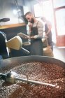 Male coffee roaster using digital tablet behind roasting coffee beans — Stock Photo