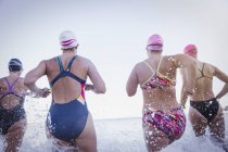 Vista trasera Nadadores activos femeninos corriendo en el océano al aire libre - foto de stock