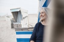 Sorridente donna anziana guardando lontano sulla spiaggia — Foto stock