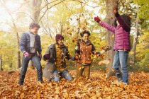 Juguetona familia joven lanzando hojas en los bosques de otoño - foto de stock