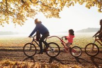 Padre e hija montar en bicicleta con remolque en el soleado parque de otoño - foto de stock