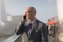 Бизнесмен разговаривает по мобильному телефону на солнечном городском мосту, Лондон, Великобритания — стоковое фото