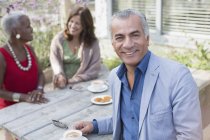 Портрет улыбающийся пожилой мужчина пьет кофе с друзьями за столом во дворе — стоковое фото